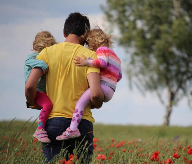 A young father carries his two little girls through a field of poppies.