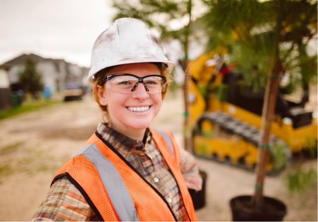A close-up of a female Foley employee wearing protective glasses and hardhat with a Caterpillar vehicle in the background.