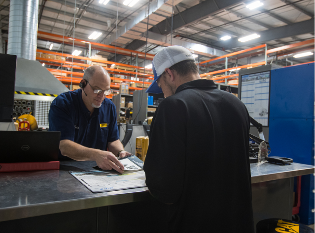 Two male Foley employees talk together as they look at a parts catalog.
