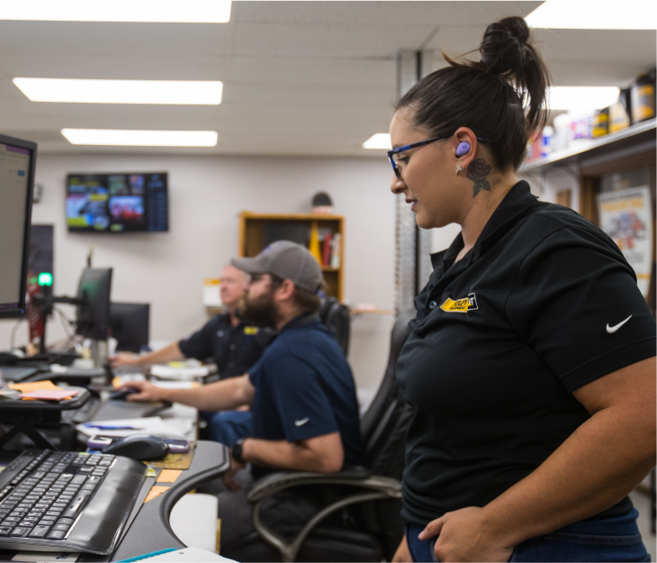 Female Foley employee working at her desk with two male employees working at their desks in the background.