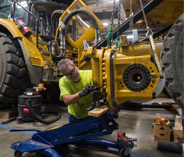 A male Foley technician wears protective gloves and glasses as he works on a large piece of Caterpillar equipment.