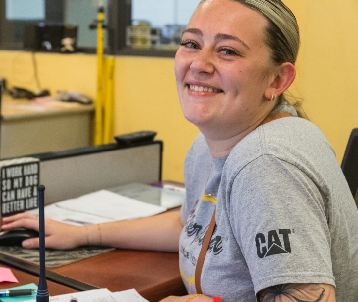 A female Foley employee is working at her desk and smiling at the camera.