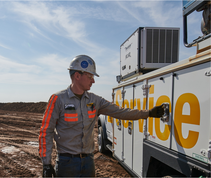 A male Foley service technician wearing a hard hat stands next to his service vehicle.