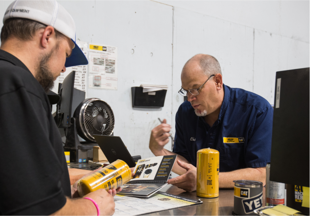 Two male Foley employees look at inventory and parts catalogs.