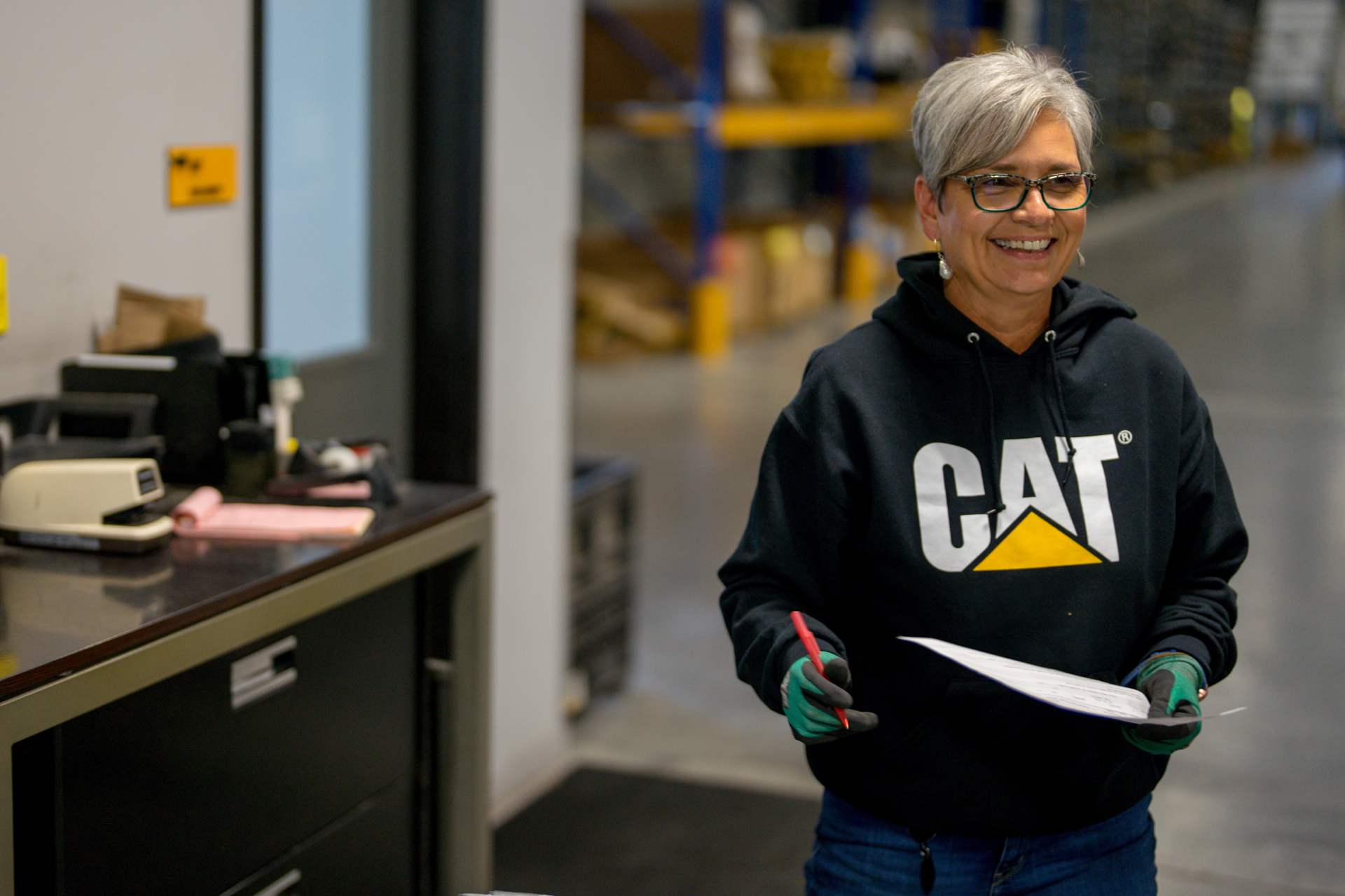 Parts employee walking in warehouse smiling with pen and packing list