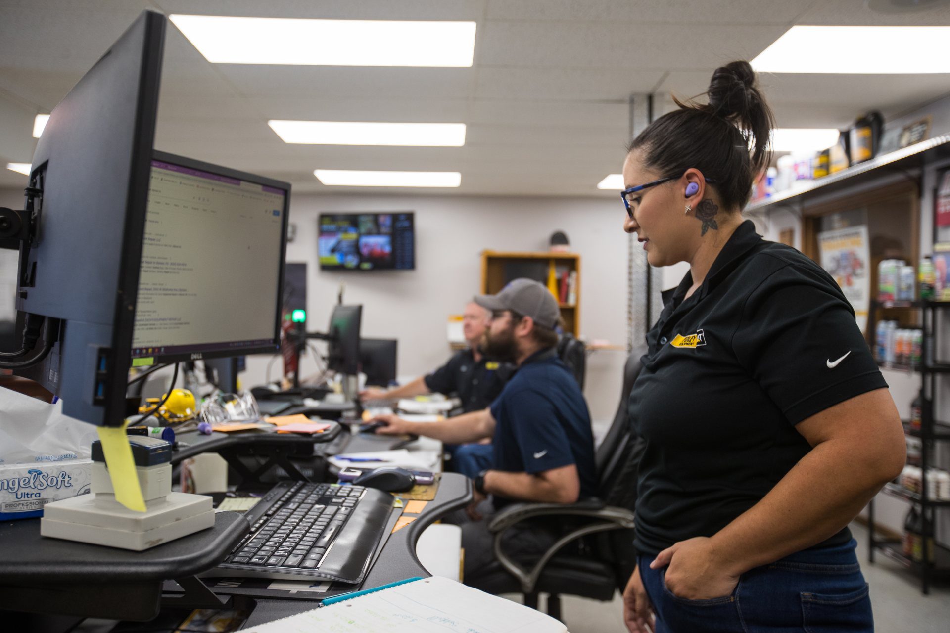 Female Foley employee working at her desk with two male employees working at their desks in the background.